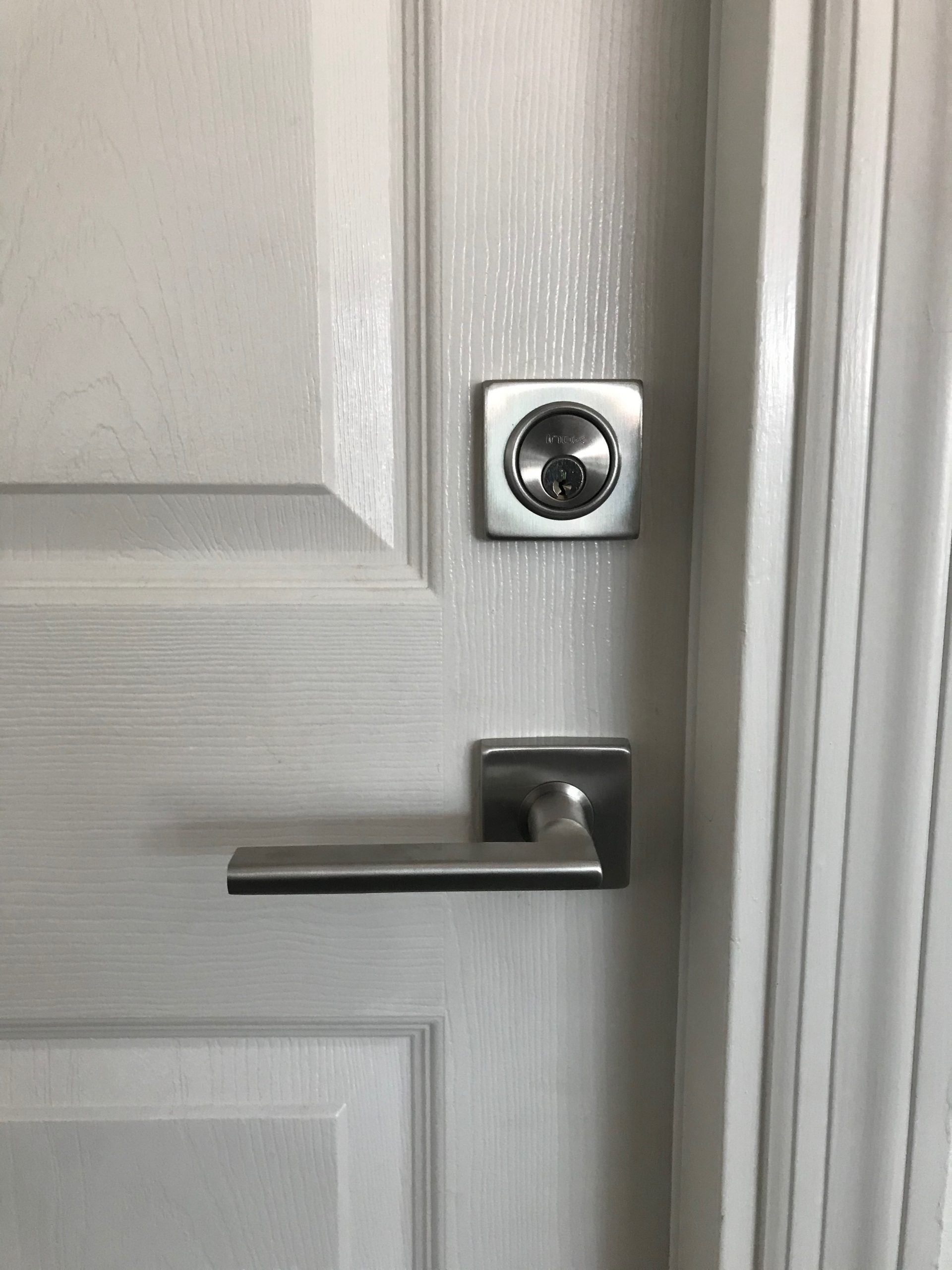 Satin nickel deadbolt and modern lever handle installed on a white door by Lockhart Locksmith in Sarasota