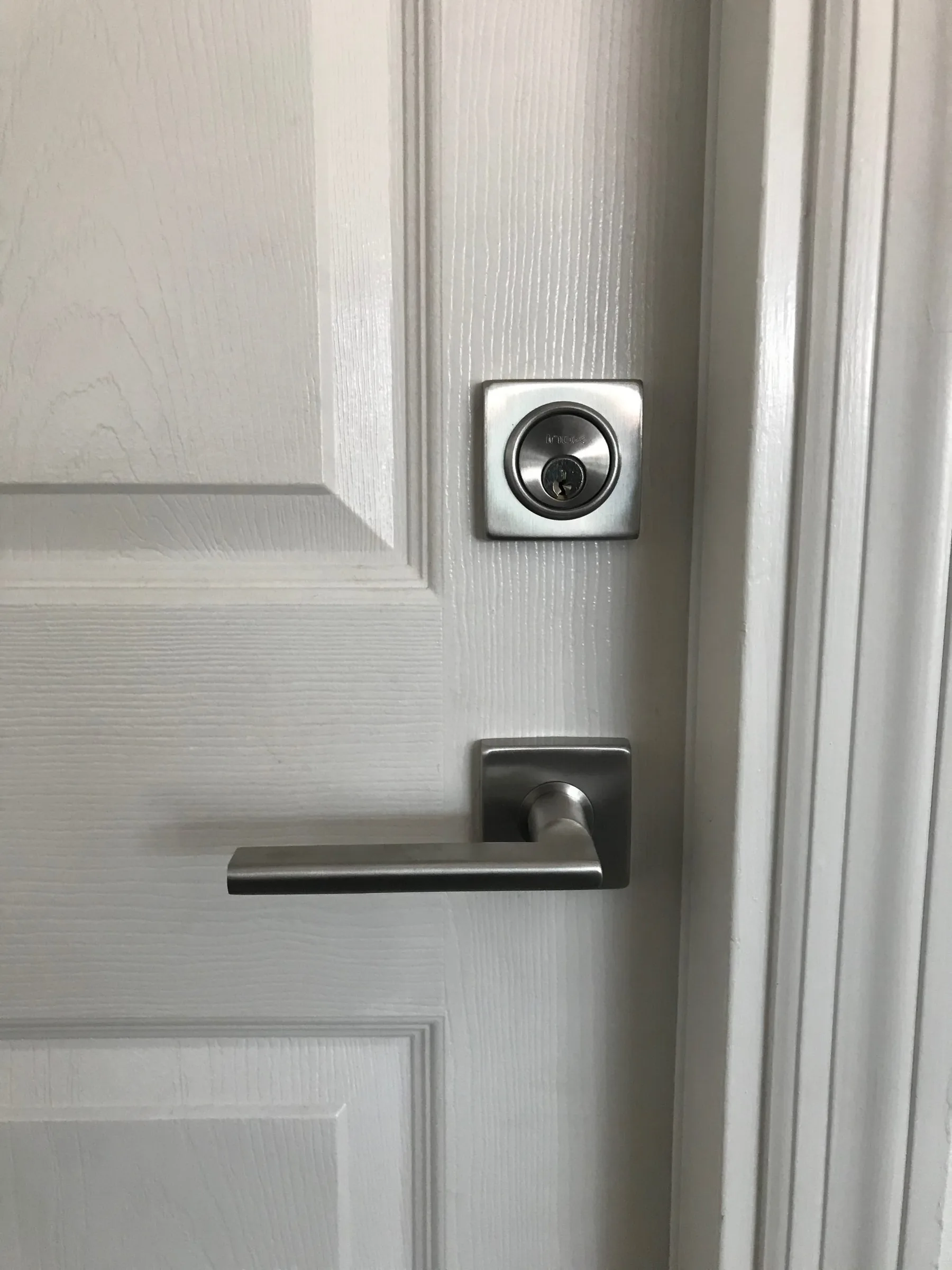 Satin nickel deadbolt and modern lever handle installed on a white door by Lockhart Locksmith in Sarasota